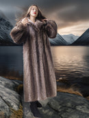 Woman in a fur coat standing on a rocky landscape with mountains and water in the background