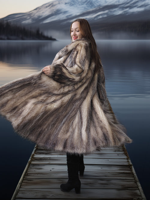 Woman in a fur coat standing on a dock with a mountainous landscape in the background