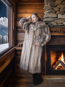Woman in a fur coat standing in a cozy cabin with a fireplace and mountain view.