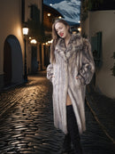 Woman wearing a fur coat on a cobblestone street at night.