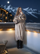 Woman in a fur coat standing on a balcony with mountains and moonlit sky in the background