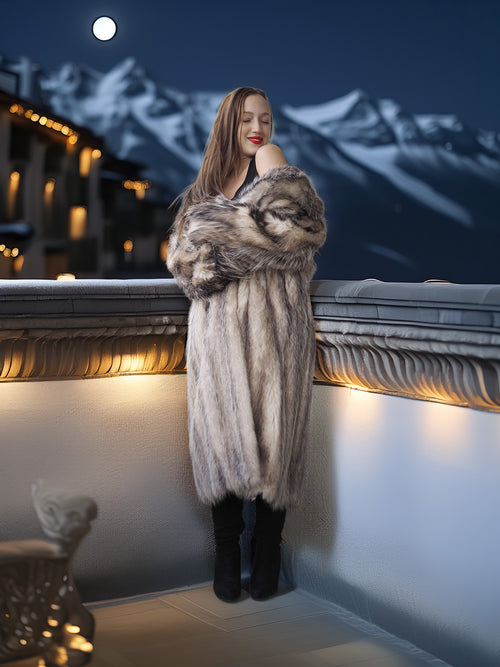 Woman in a fur coat standing on a balcony with mountains and moonlit sky in the background