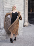 Stylish fashionable woman wearing black tank top and long tulle skirt, posing confidently on the street against a brick wall background.