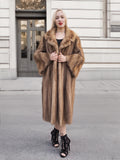 Elegant fur coat of vintage pastel brown mink, worn by a stylish woman with blonde hair standing in front of an ornate building entrance.