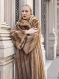 Elegant woman wearing luxurious vintage pastel Canadian brown mink fur coat with a fur-trimmed hood, posing outdoors against a historic building.