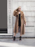 Elegant vintage Canadian mink fur coat in a pastel brown hue, worn by a fashionable woman against a white brick wall background.