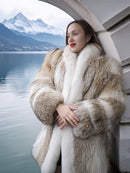 Woman wearing a fur coat with a scenic background of mountains and water.