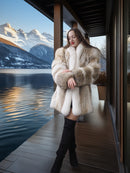 Woman in a fur coat standing on a wooden deck with a scenic mountain and lake view.
