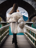 Person wearing a fur coat walking on a bridge with a snowy landscape in the background