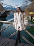 Woman in a fur coat standing on a wooden bridge with mountains in the background