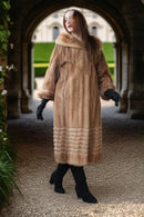 Tan mink fur long coat with hood and ribbed hem, seen full length with black boots