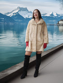 Woman in a fur coat standing by a lake with mountains in the background