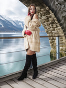 Woman in a fur coat and red gloves standing on a wooden deck with a scenic background