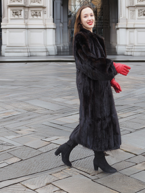 Smiling woman in full-length black mink fur coat, walking confidently. Warm and stylish fur fashion for winter seasons.