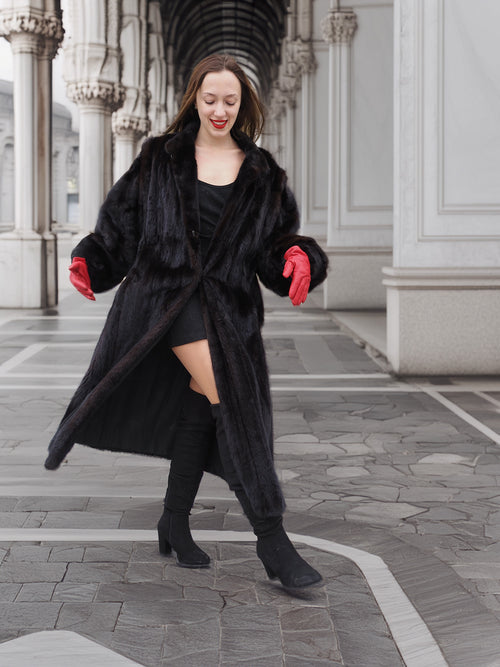 Model twirling in black mink fur coat with red gloves, showing coat’s volume and flow. Premium winter fashion outerwear.