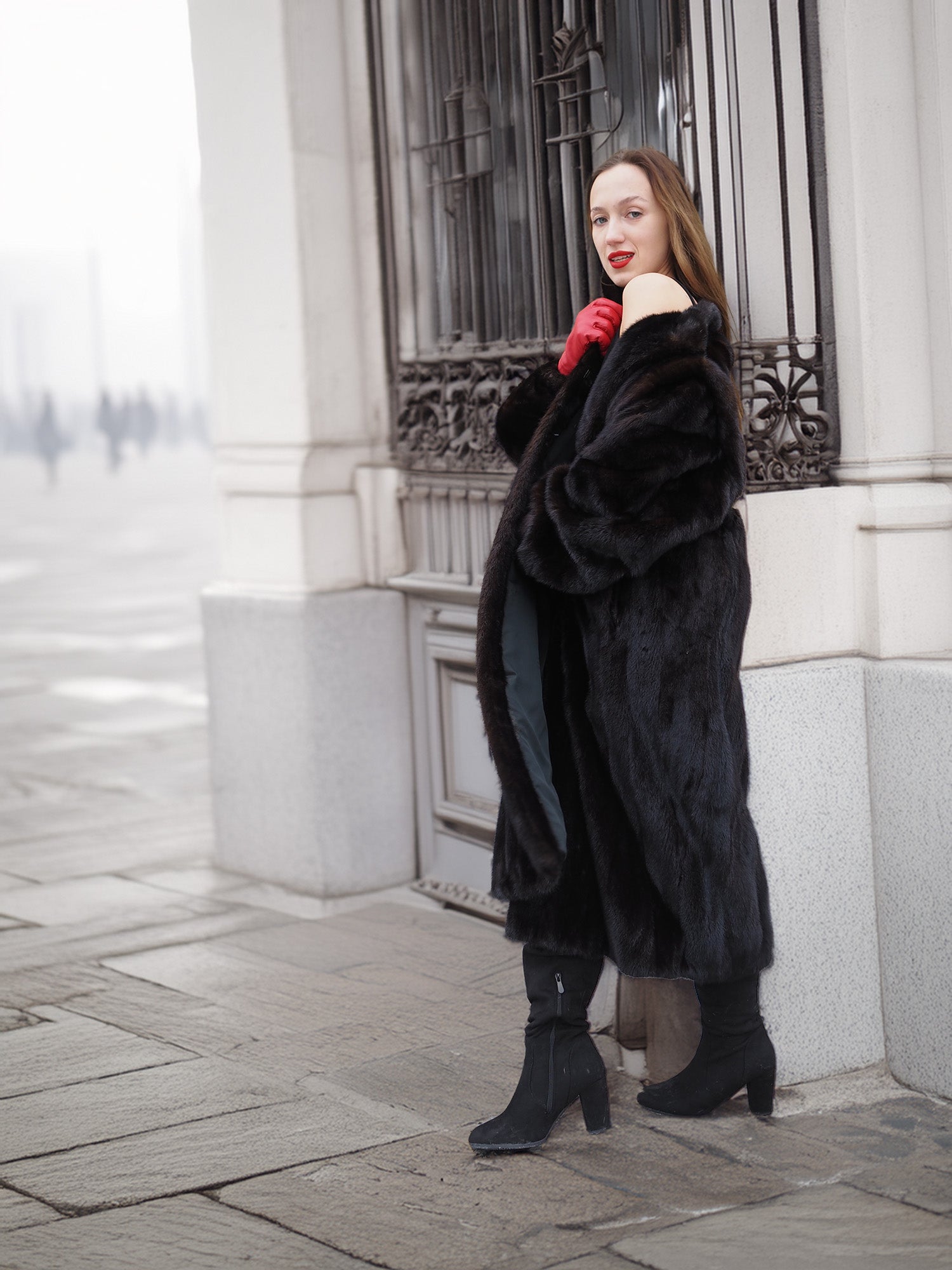 Model posing in black mink fur coat near ornate window. Classic design with luxurious texture and winter-ready style.