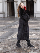 Woman in dark ranch black mink fur coat walking on cobblestone path. Elegant and warm outerwear for cold-weather fashion.