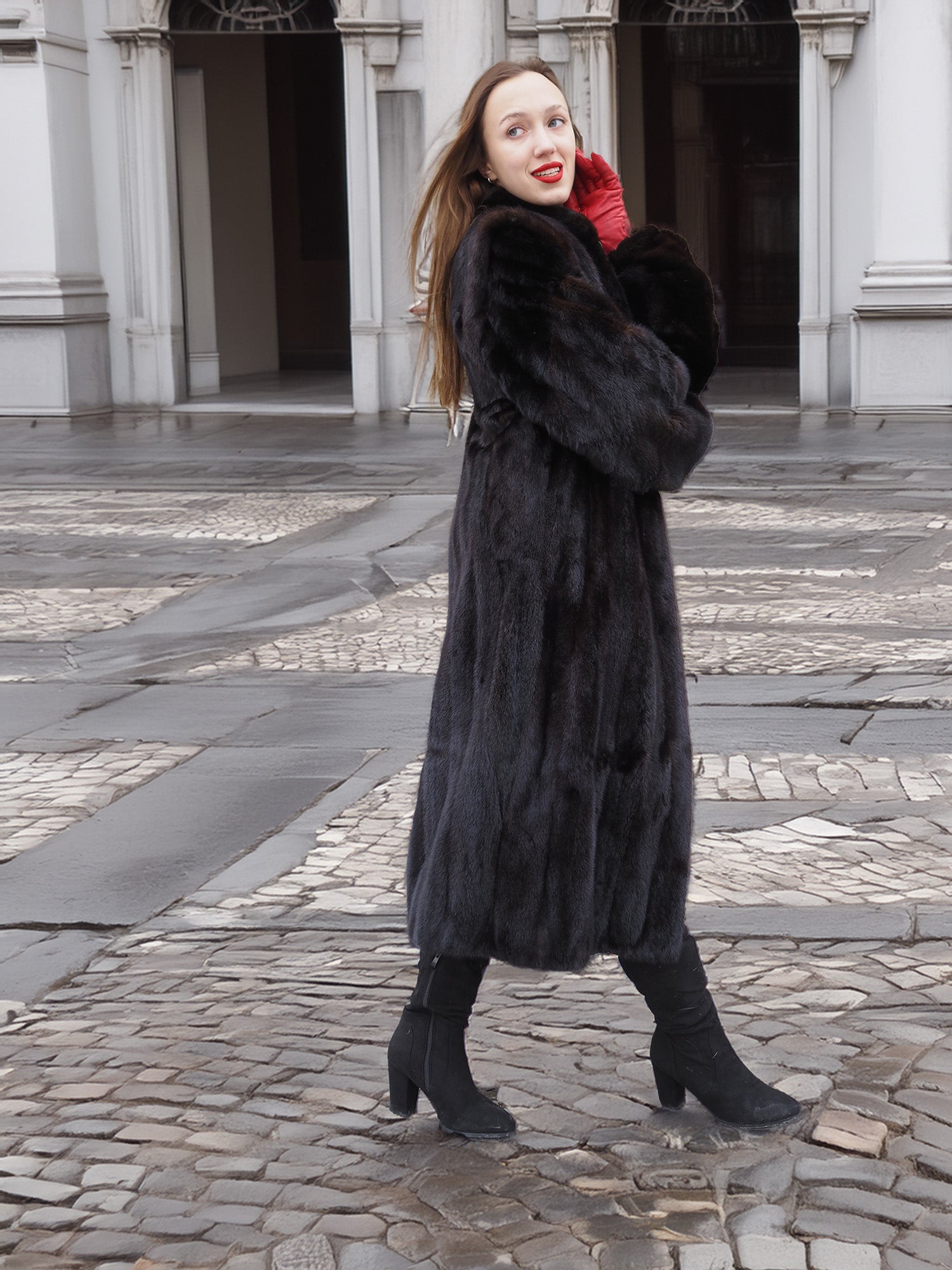 Woman in dark ranch black mink fur coat walking on cobblestone path. Elegant and warm outerwear for cold-weather fashion.