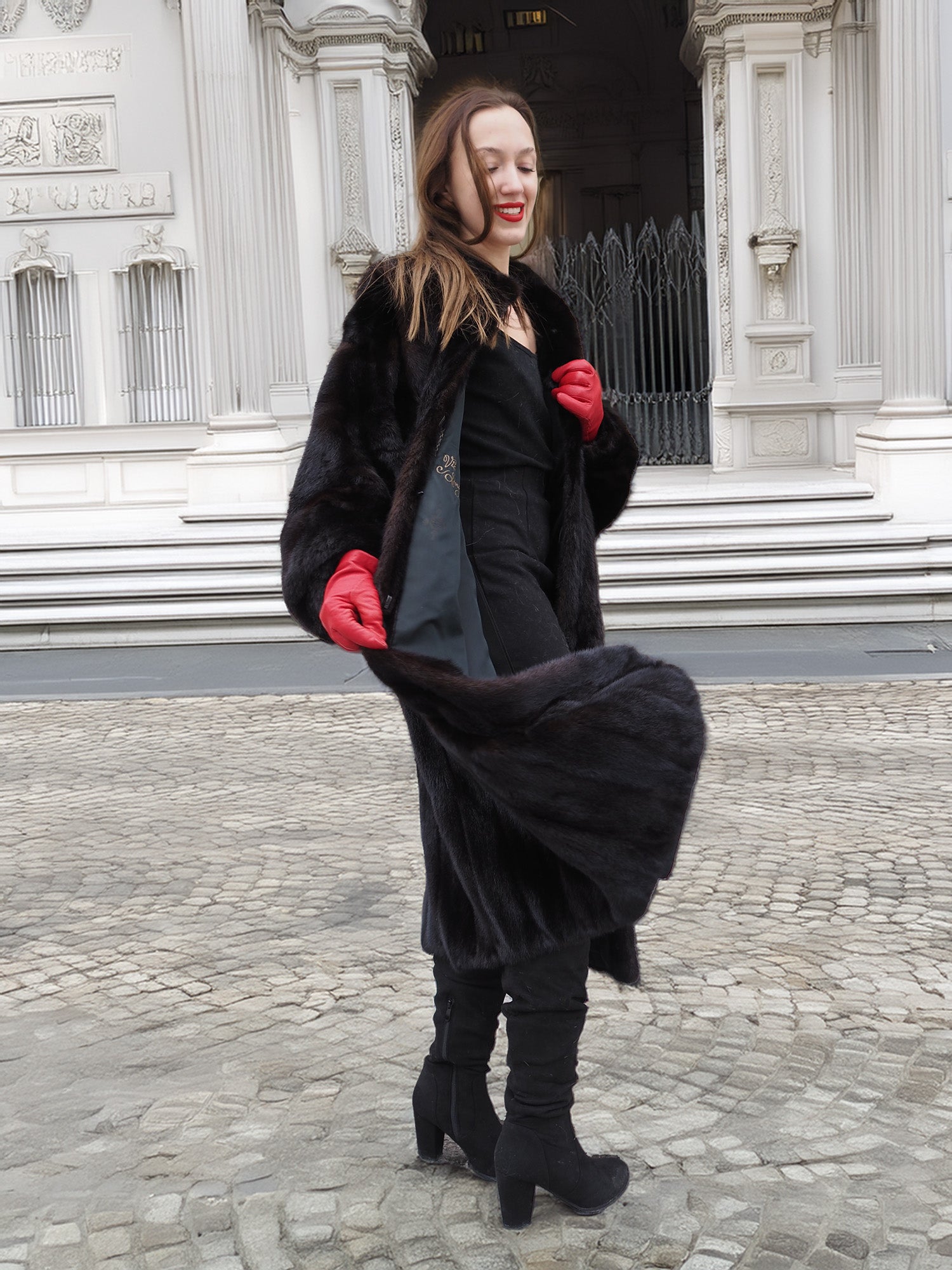 Model in black mink fur coat with red gloves, mid-step. Classic full-length fur coat for luxury winter fashion collections.