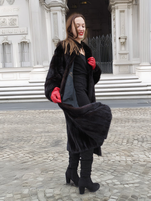 Model in black mink fur coat with red gloves, mid-step. Classic full-length fur coat for luxury winter fashion collections.