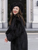 Smiling woman in black mink fur coat and hat, showing the coat’s soft texture and classic cut. Luxury winter fashion statement.