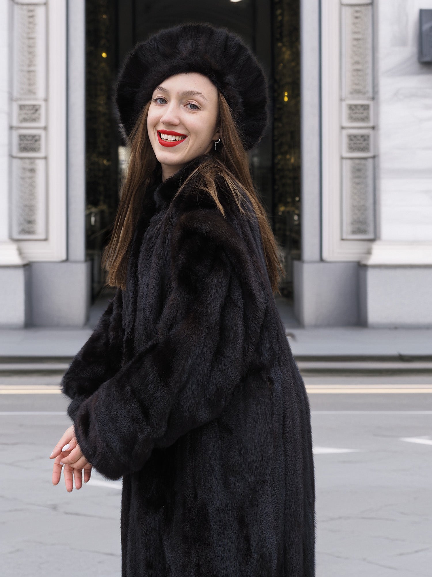 Smiling woman in black mink fur coat and hat, showing the coat’s soft texture and classic cut. Luxury winter fashion statement.
