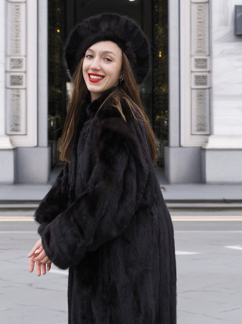 Smiling woman in black mink fur coat and hat, showing the coat’s soft texture and classic cut. Luxury winter fashion statement.