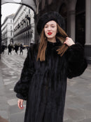 Woman wearing a dark ranch black mink fur coat with small round collar and matching hat. Stylish and warm outerwear for winter fashion.