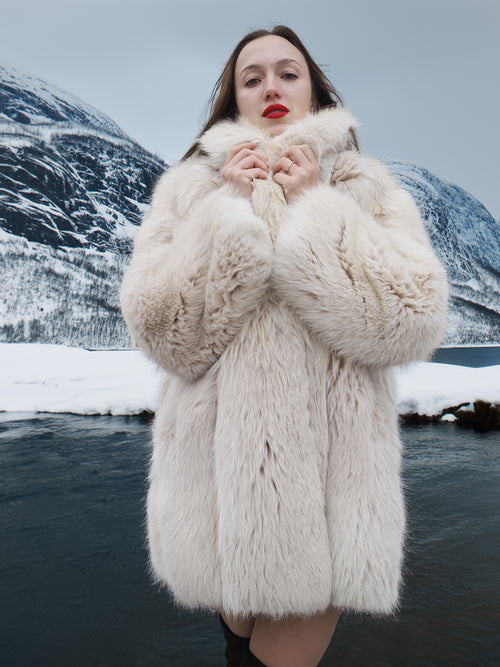 Soft Plush Blush Fox Jacket S/M styled in front of a snowy river, emphasizing thick fur and luxurious winter outerwear.