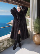 Woman in a long black fur coat standing on a balcony with ocean view
