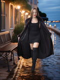 Woman in a black coat and dress walking along a waterfront at dusk.