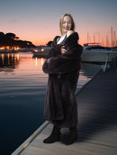 Woman in a fur coat standing on a dock at sunset.