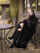 Woman in a black fur coat sitting outdoors near a table with a glass of wine.