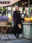 Woman in a long black coat walking past a market stall with lavender and oranges.