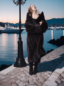 Woman in a fur coat standing by a waterfront at dusk