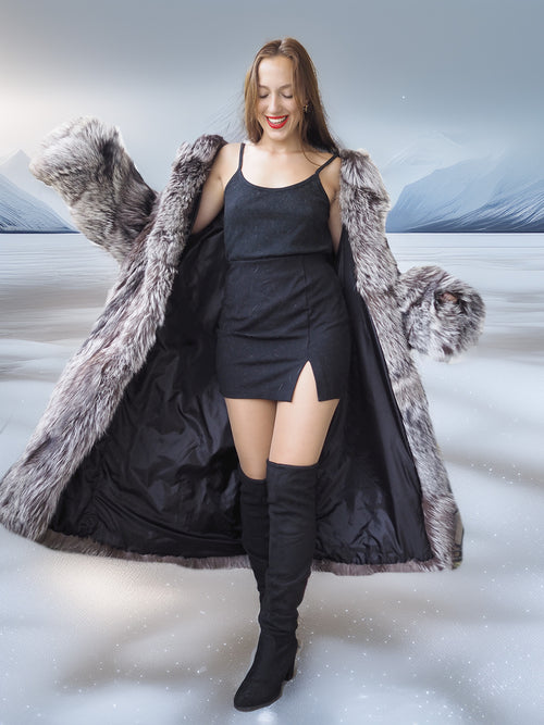 Woman wearing a long fur coat over a black dress and boots in a snowy landscape.