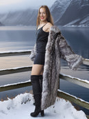 Woman in a fur coat standing by a snowy landscape with mountains.