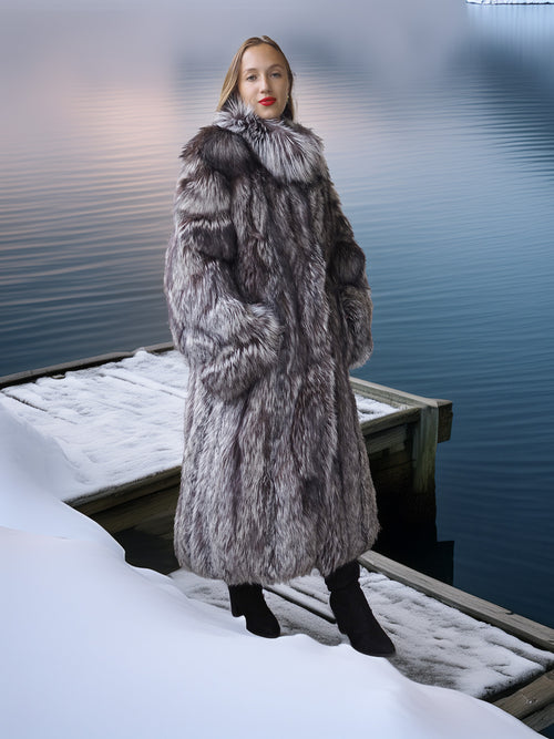 Person wearing a fur coat standing on a snowy dock with water in the background
