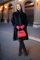 Woman in a black coat and red gloves holding a red handbag on a city street.