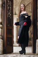 Woman in a black dress and coat standing in an archway with stone walls.