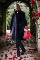 Woman in a black coat and red gloves holding a red handbag, standing under a floral arch with red flowers.