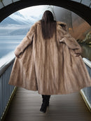 Person wearing a fur coat walking on a bridge with a scenic view in the background
