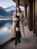 Woman in a fur coat standing on a wooden deck with mountains and water in the background