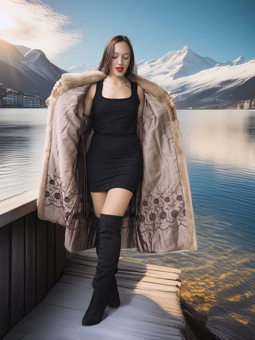 Woman in a long coat standing on a dock with mountains and water in the background