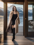 Woman in a long coat standing in front of a door with a mountain view.