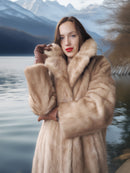 Woman wearing a fur coat standing by a lake with mountains in the background