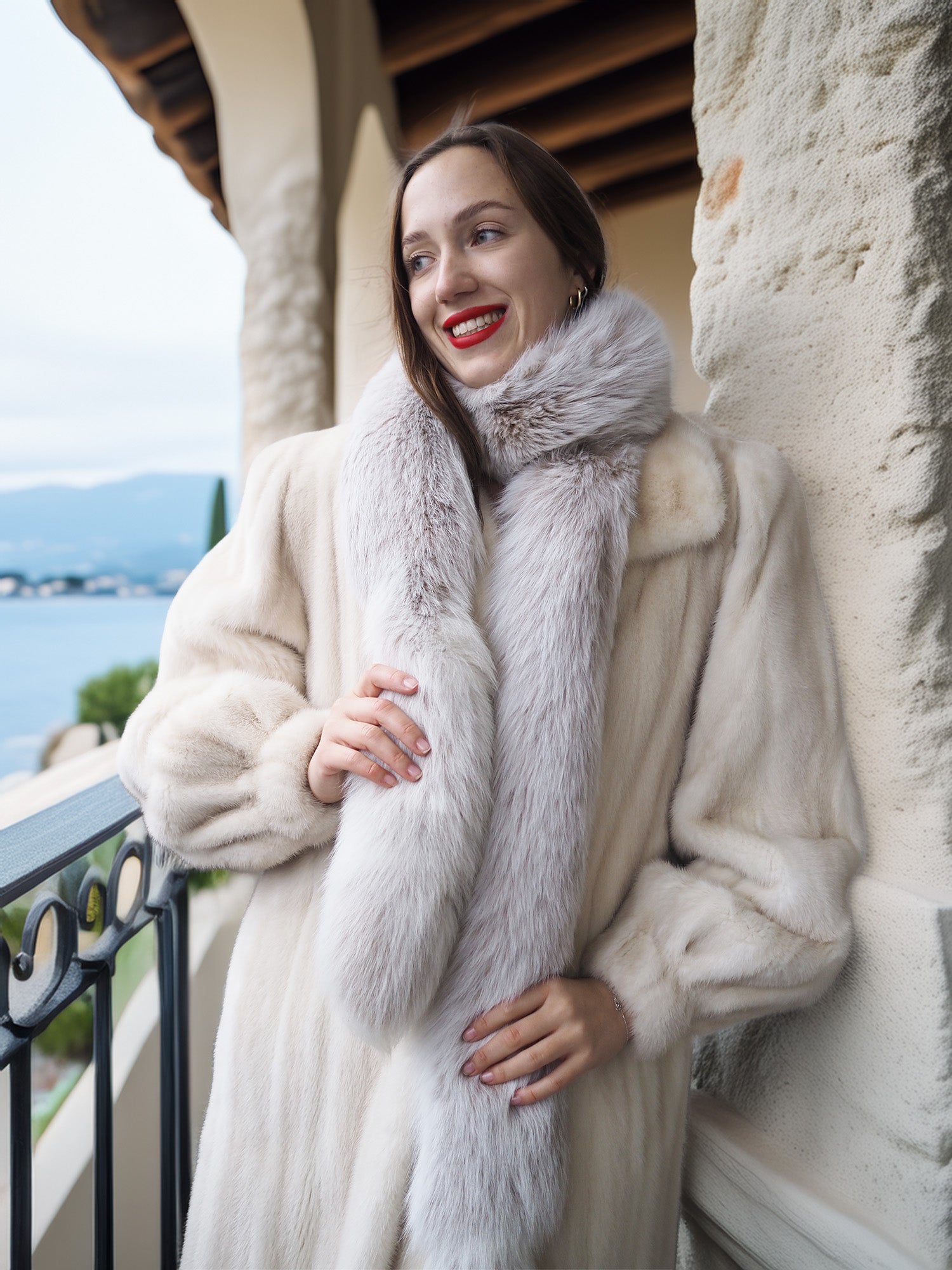 Woman wearing a fur vest and coat on a balcony with scenic background