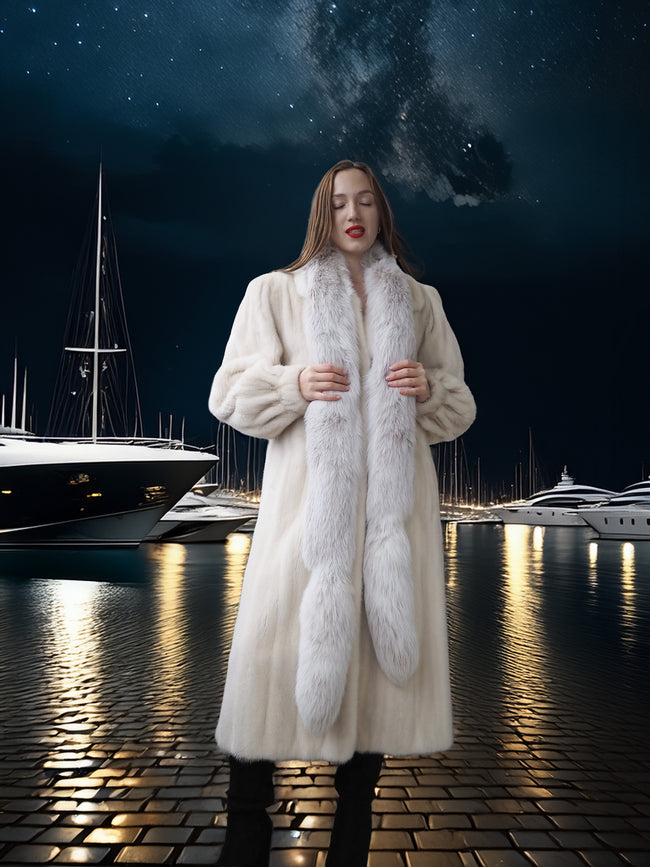 Woman in a long white coat with a fur scarf standing on a dock at night.