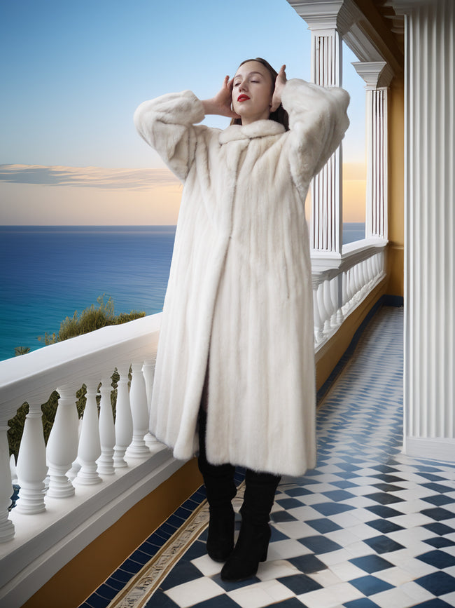 Woman in a white fur coat standing on a balcony with ocean view