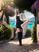 Woman in a black dress and white coat standing on a cobblestone path with a scenic background.